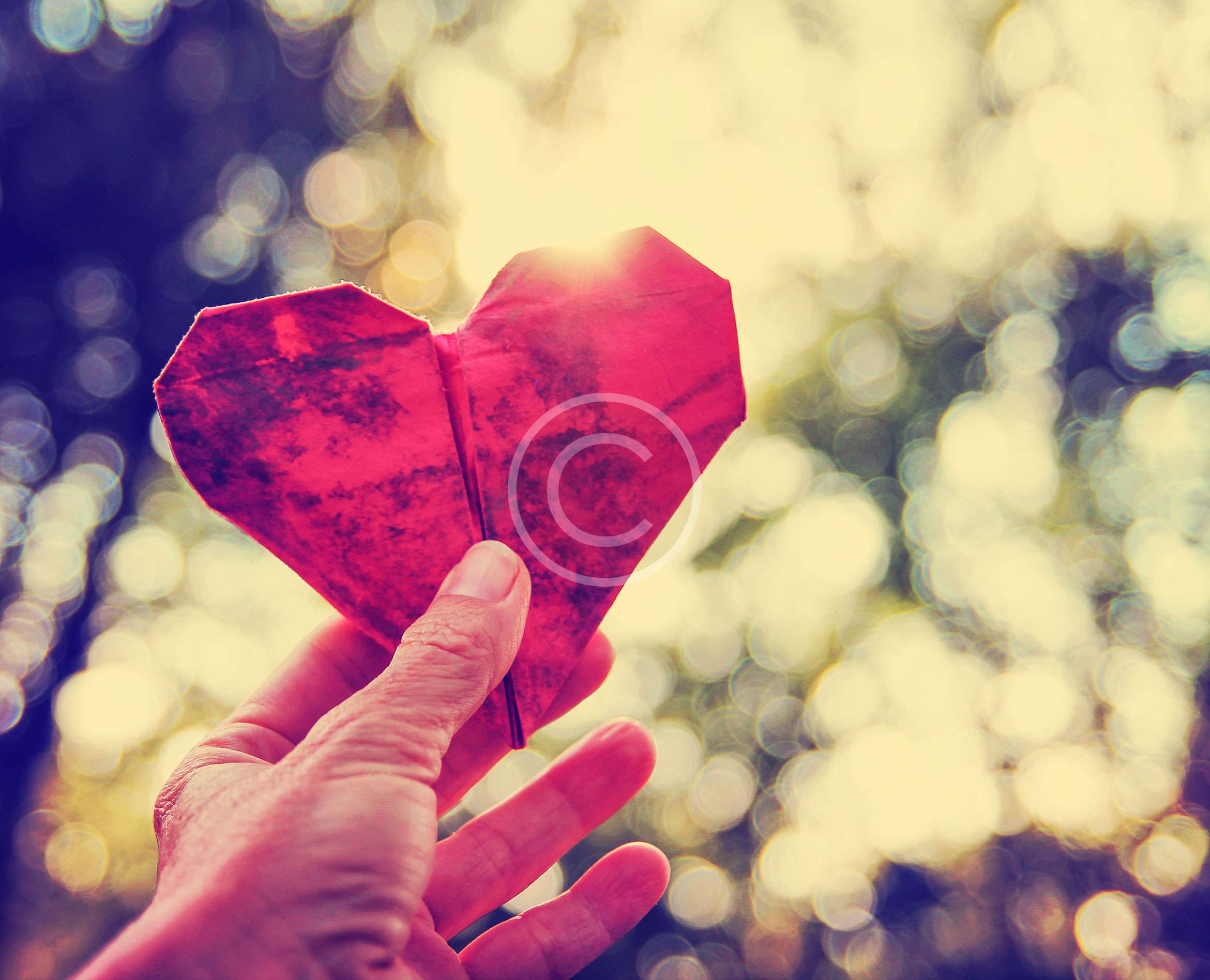 A hand holding up a red paper heart